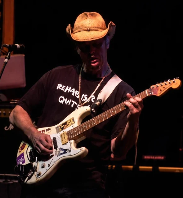 The Ducks' guitarist in a straw cowboy hat, playing a white electric guitar